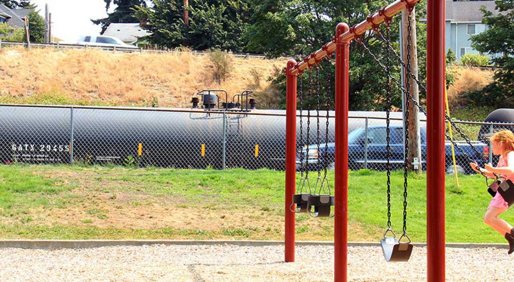 an oil train rolls by a girl on a swing set