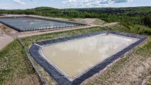 LNG wastewater holding site: A series of large, rectangular ponds lined with plastic barriers. The ponds are filled with water, some machinery and pumps can be seen at the edges. The surrounding area appears industrial.
