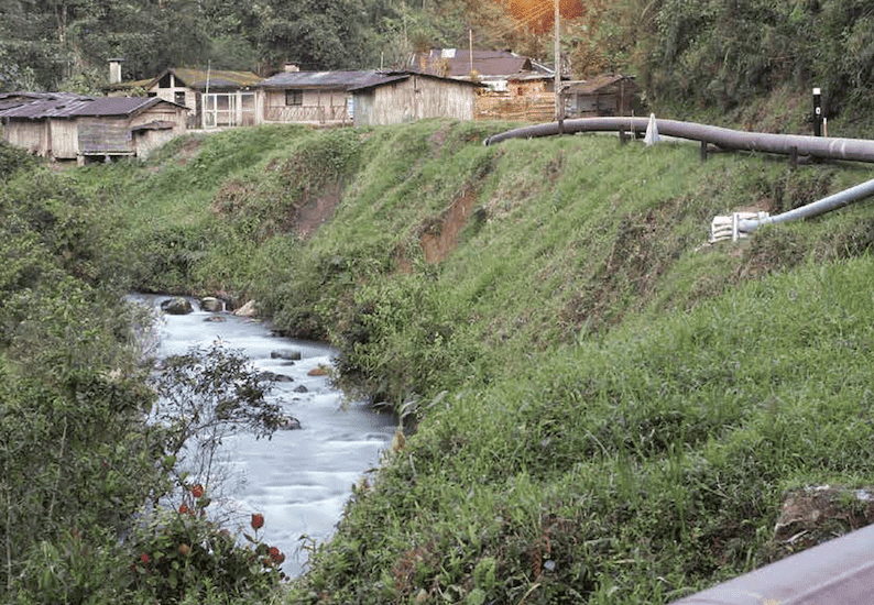Pipeline running through the Amazon rainforest above a river with white text over red background on the top left corner
