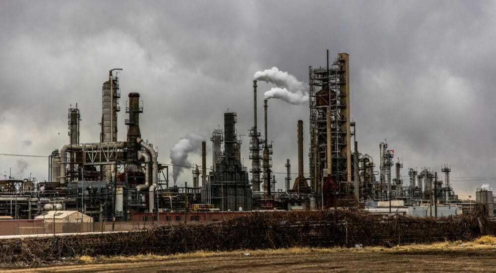 Fossil fuel processing factory with multiple smoke stacks, with a grey sky in the background.