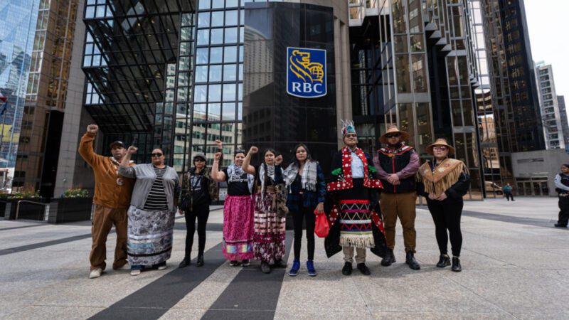 A group of a dozen Indigenous and frontline land defenders with fists raised, outside of RBC's HQ in Toronto