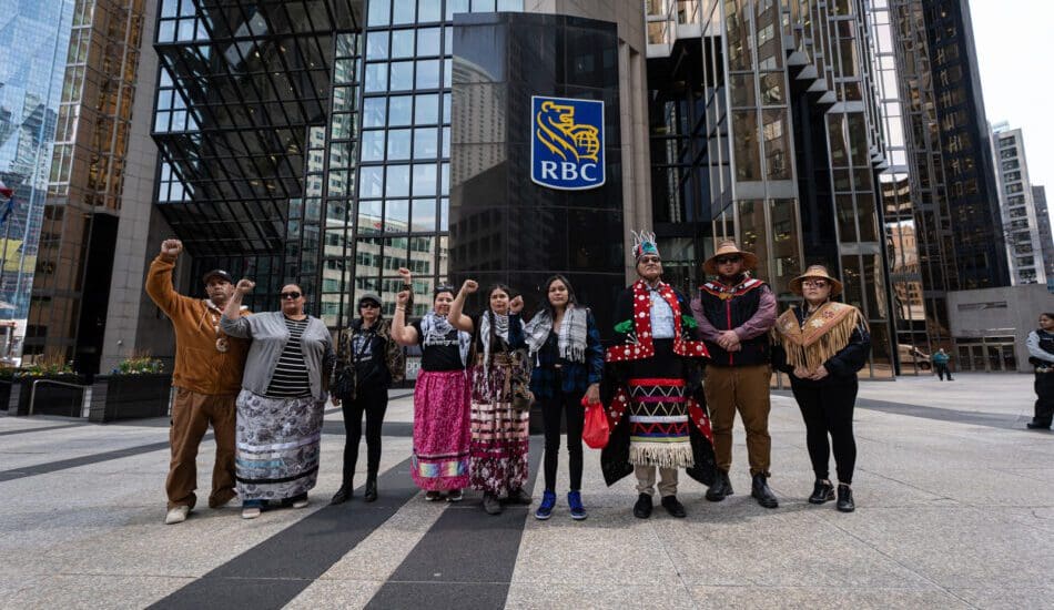 A group of a dozen Indigenous and frontline land defenders with fists raised, outside of RBC's HQ in Toronto