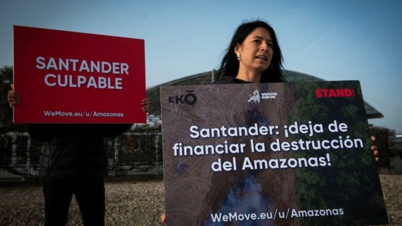 Two people holding posters outside the Santander AGM.